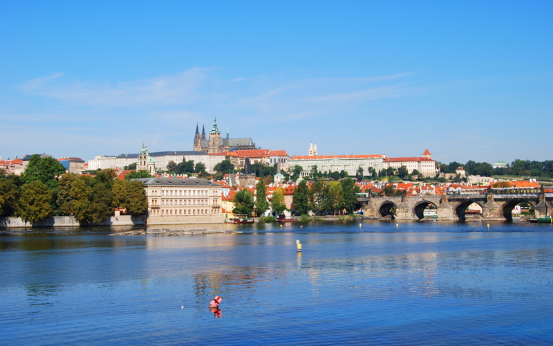 18 - A scenic view of the Vltava River in Prague, Czech Republic, featuring the historic Prague Castle and part of the Charles Bridge under a clear blue sky
